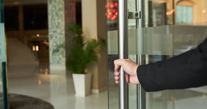 A man wearing a black suit is holding a glass door open