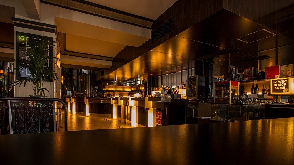 An interior view of a fancy restaurant with lighting under the bar table and black stools up against the bar
