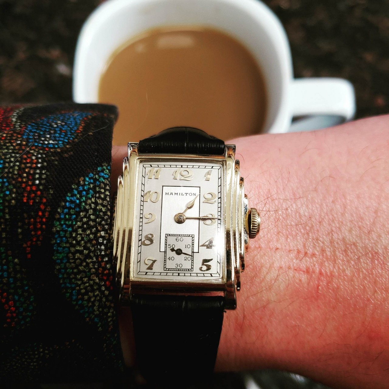A 1933 Hamilton Putnam watch has a gold case in an art-deco stepped style case. The dial is white with gold indices and matchind gold hands. It is on a black leather strap