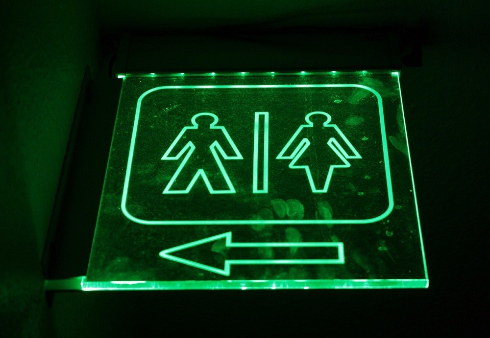 A neon green sign points to the locations of a bathroom inside a dimly lit restaurant