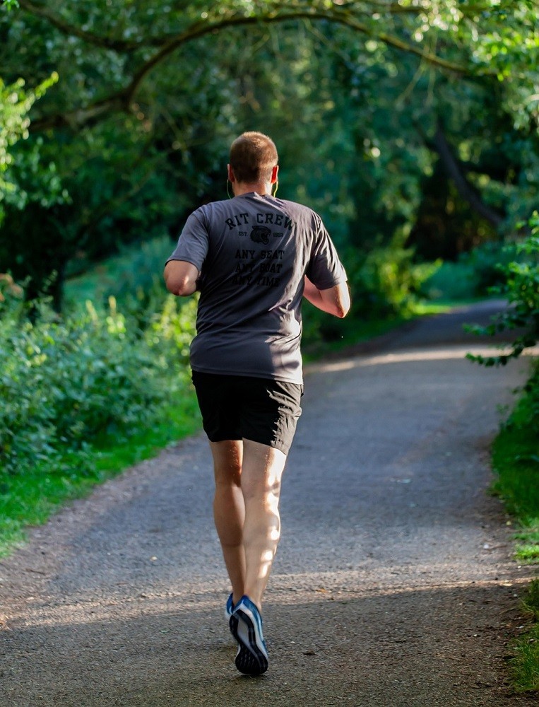 A middle aged man is running down a gravel road. He is very fit