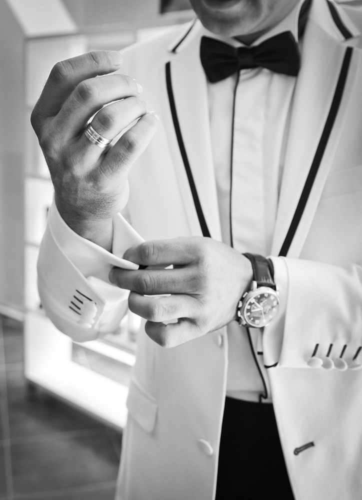 A man wearing a white tuxedo with black trim is adjusting his jacket cuff
