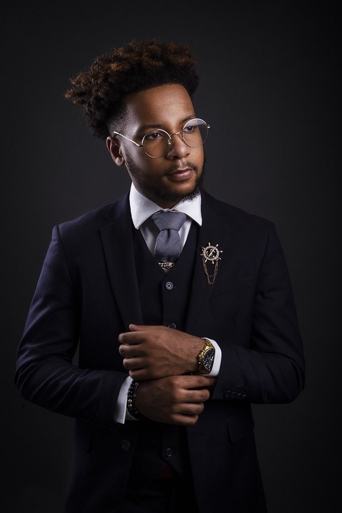 A man wearing a black suit, blue tie, white dress shirt, and nice dress watch is looking at something out of frame. He looks very confident