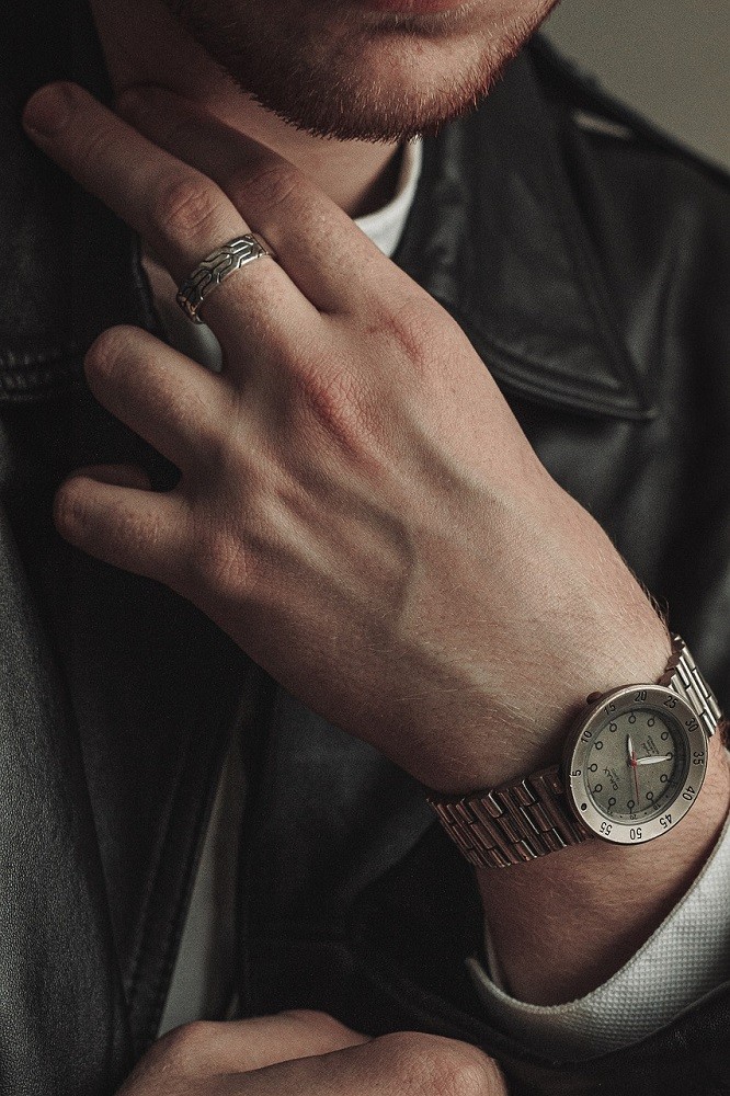 A man is wearing a silver ring and a simple dress watch on the same hand, which shows that a few simple items can look really good together