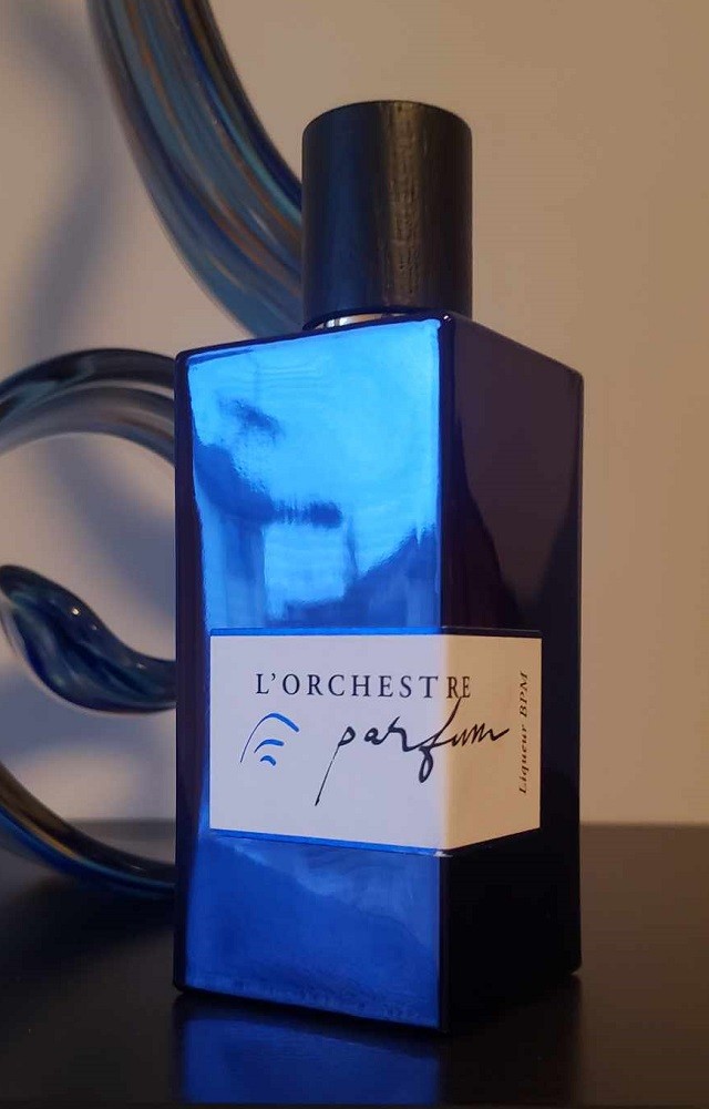 A blue, reflective, rectangular bottle of cologne has a white label with the brand and name of cologne on it. It comes with a black wooden cap