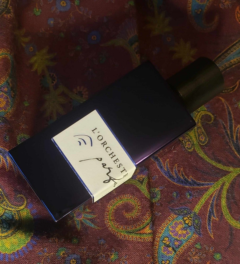 A bottle of L'Orchestre Parfum Liqueur BPM sits on a red cravat with a blue/green paisley pattern on it