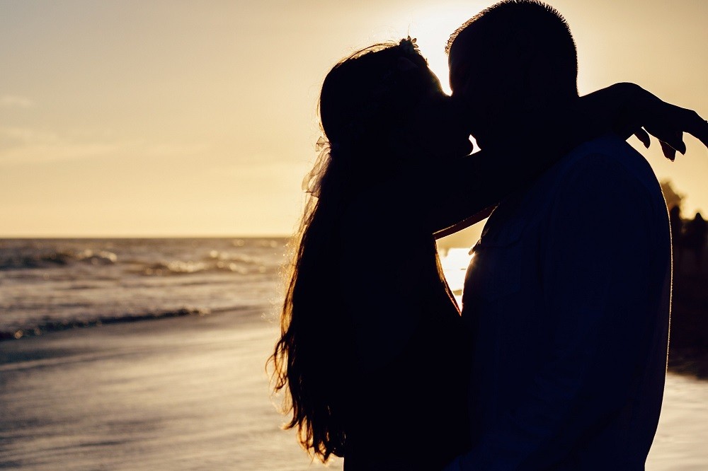A man and woman kiss in front of crashing waves on a beach