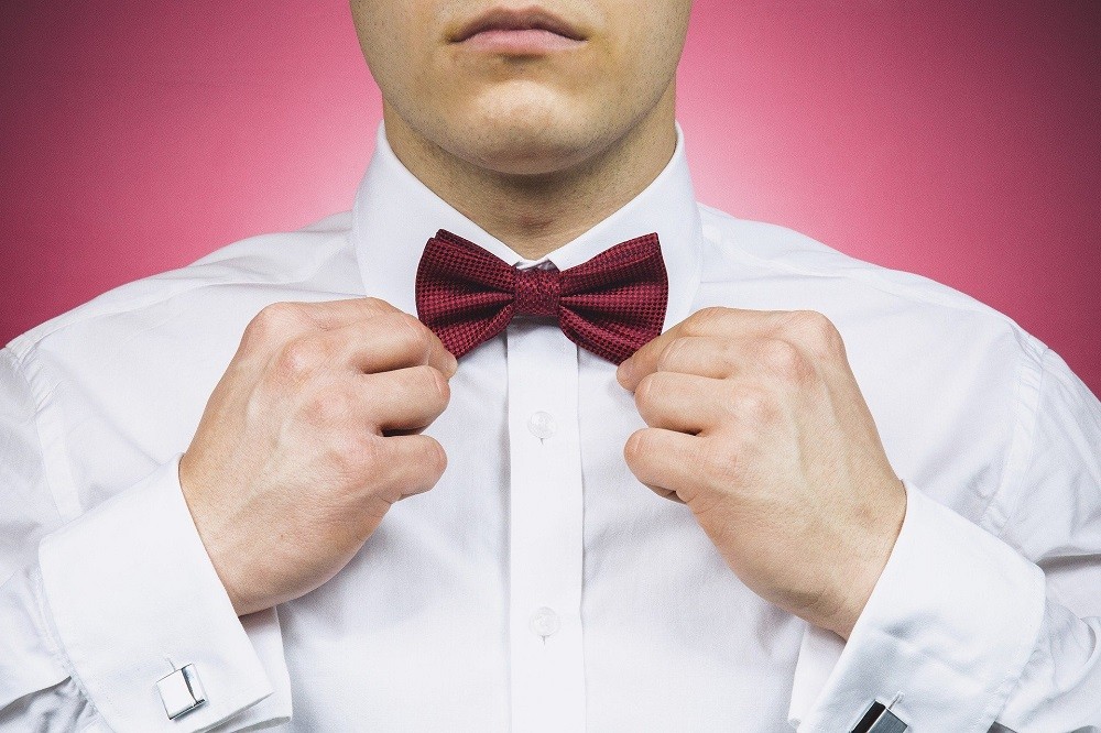 A man adjusts his red velvet bow tie
