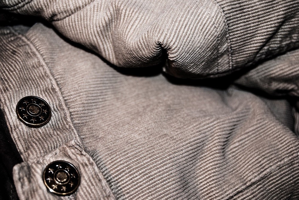 A pair of grey corduroy pants sit loosely folded on a desk