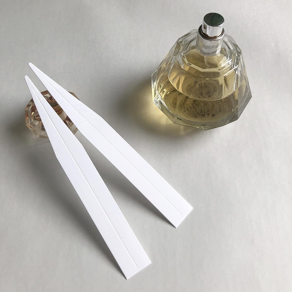 A small decanted bottle of perfume sits beside two paper test strips, a method used in testing fragrances