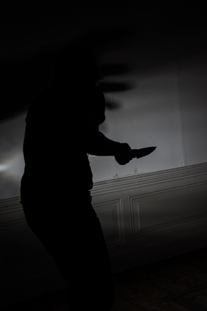 A suspicious character is hiding in the shadows. They are brandishing a knife and sneaking around a corner