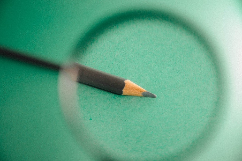 A sharpened pencil is under a magnifying glass, symbolizing the importance of fine details
