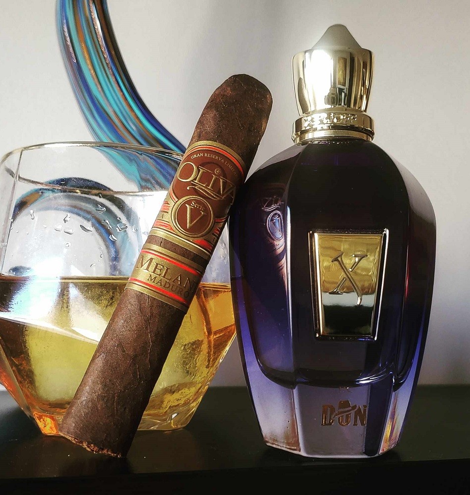A bottle of Don by Xerjoff sits with a cigar and glass of whisky beside it