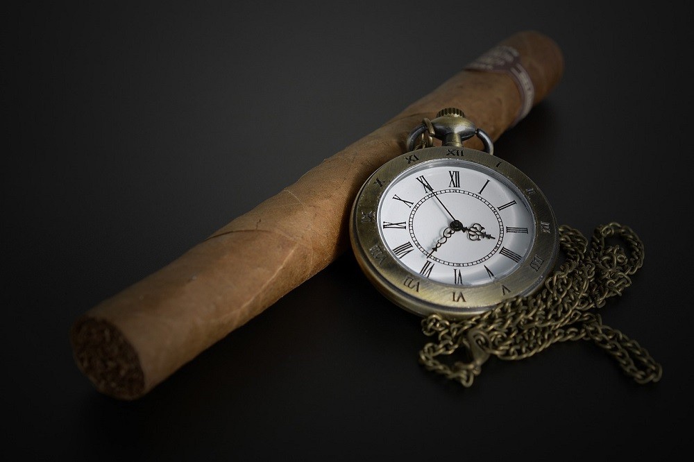 A gold pocket watch is resting against a cigar