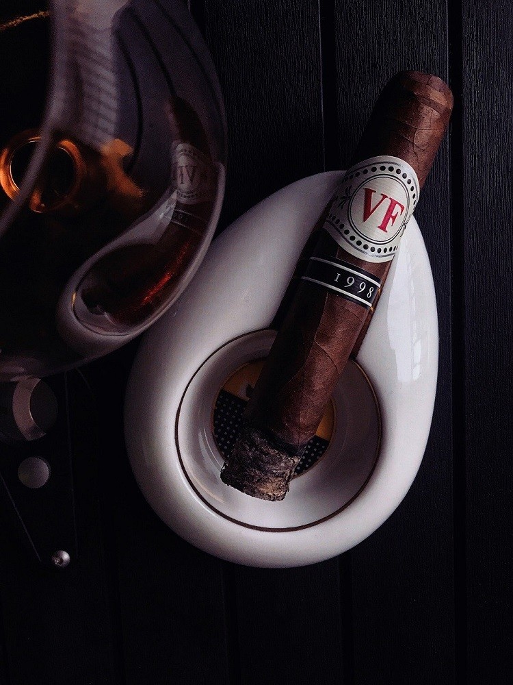 A lit cigar sits inside a white ashtray