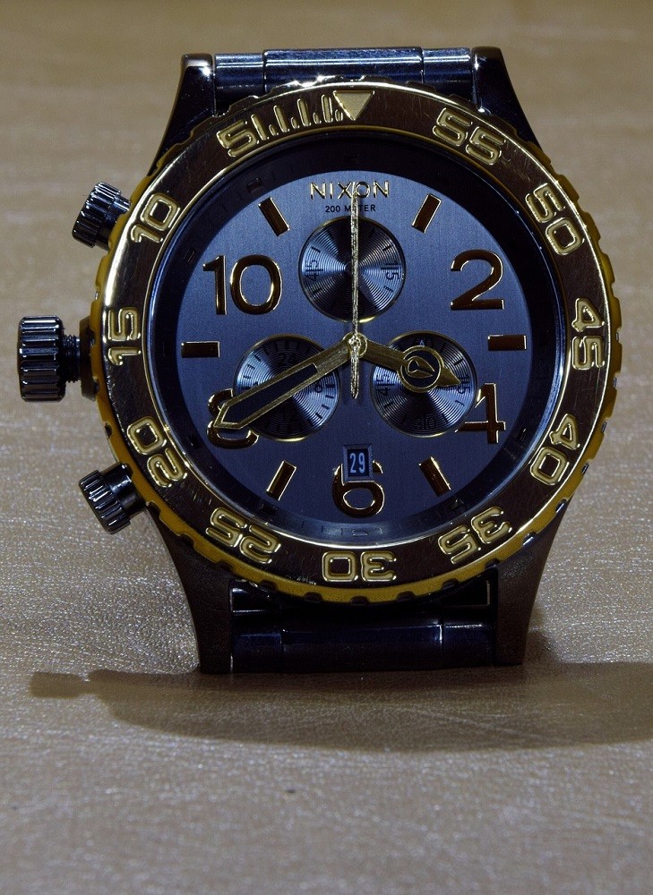 A blue and gold Nixon watch has the crown pulled out