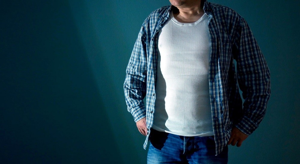 A man wearing a white undershirt is buttoning up his dress shirt