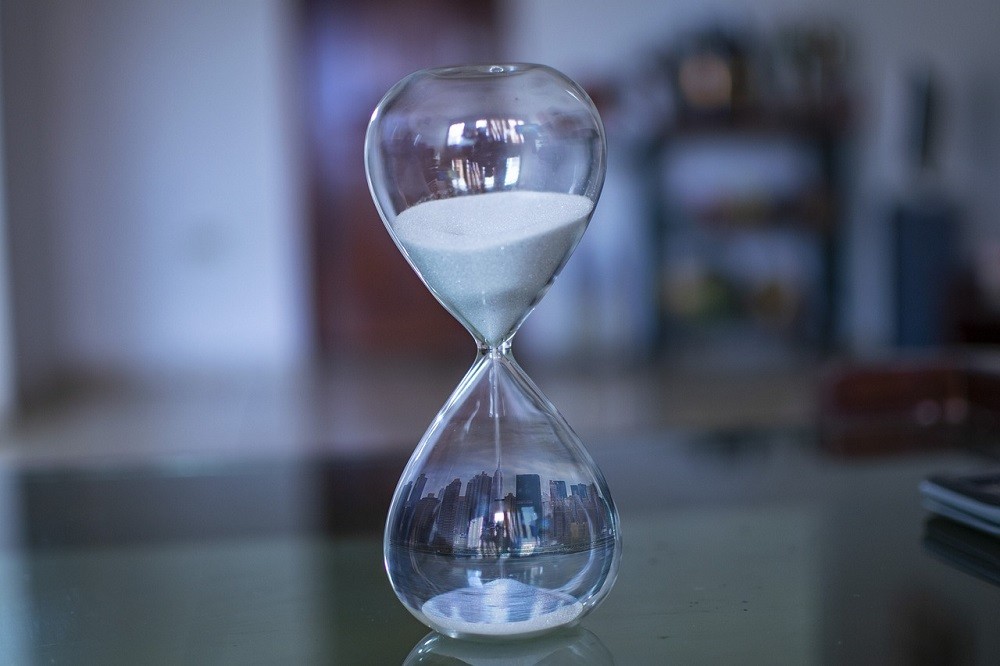 An hourglass sits on the counter with white sand pouring from the top chamber into the bottom. It represents how time moves fluidly