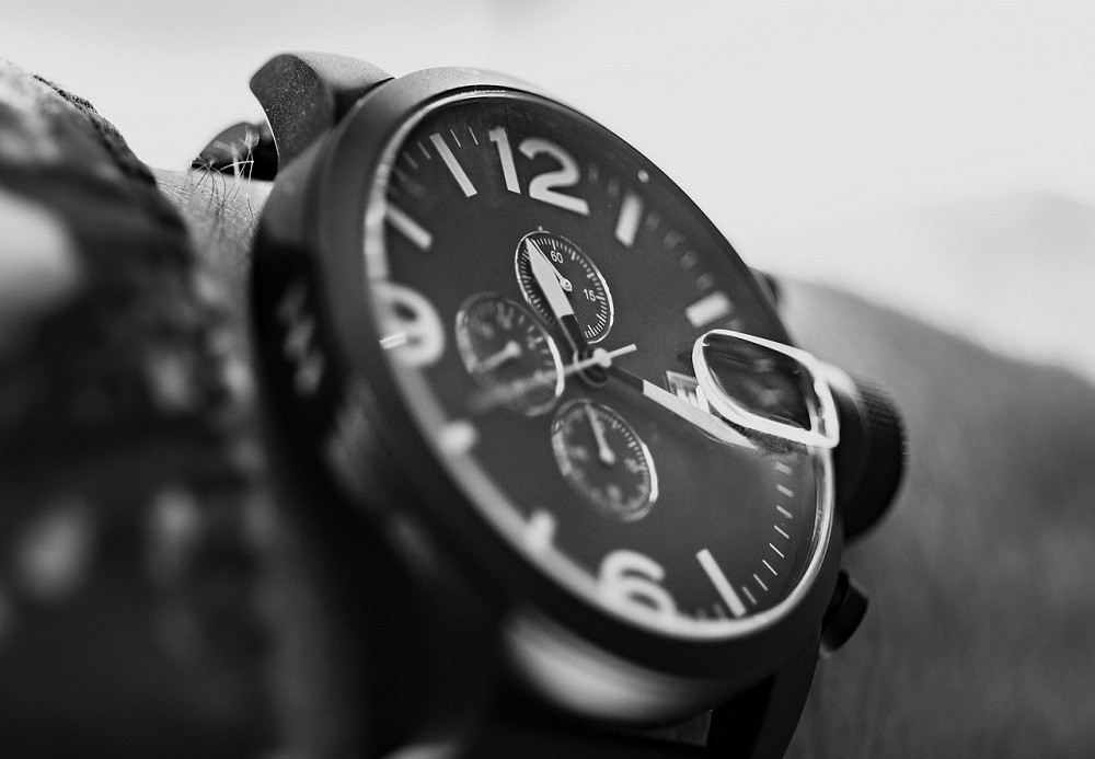 A black and white photograph of a black wrist watch with white numerals on someones wrist