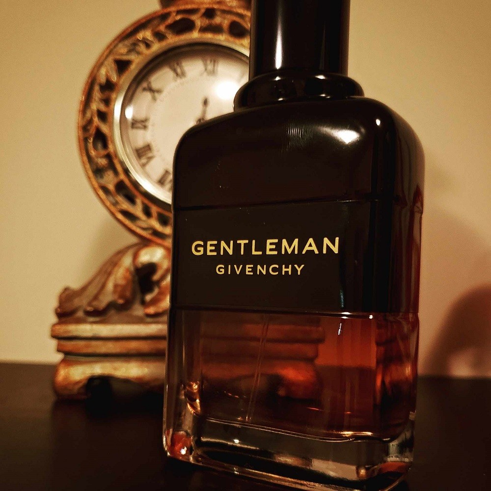 A dark brown bottle of Givenchy is on a table in front of a gold clock decoration