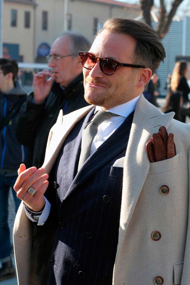 A man wearing a white jacket has his brown winter gloves nested in the breast pocket