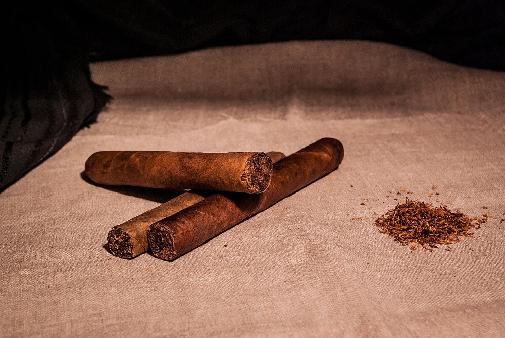 Three freshly rolled medium brown cigars sit on a white cloth