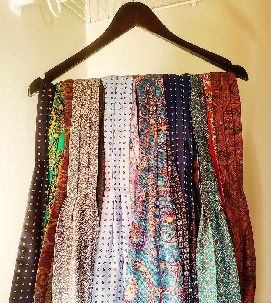 Many ascots/cravats are hung on a cloths hanger. Each ascot/cravat has its own unique colour palate, pattern, and design