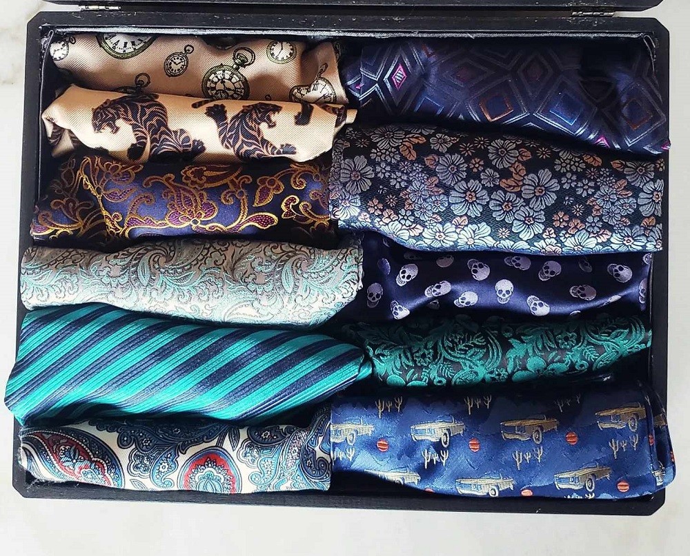 10 ascots/cravats with various designs in many different colours are neatly rolled and stored in a box