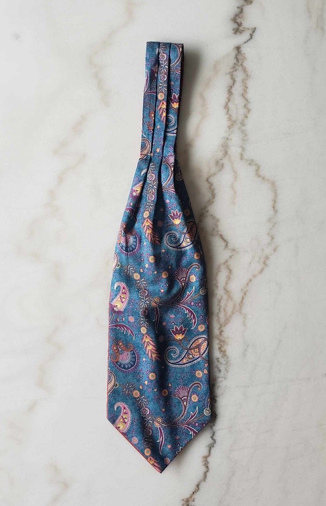 A blue ascot with an orange and purple paisley pattern is laid flat on a table