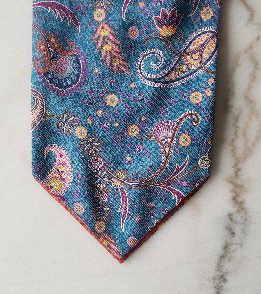 A blue ascot with an orange and purple paisley pattern is on a table