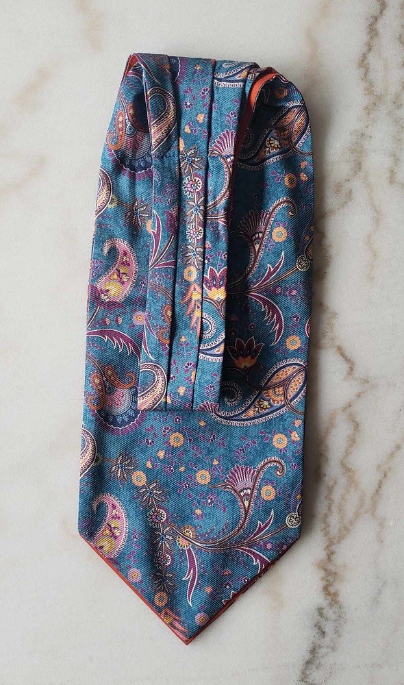 The narrow end of a blue cravat with an orange and purple paisley pattern is neatly folded over itself