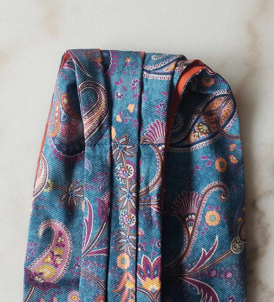 A blue ascot with orange and purple paisley patterns is folded in half
