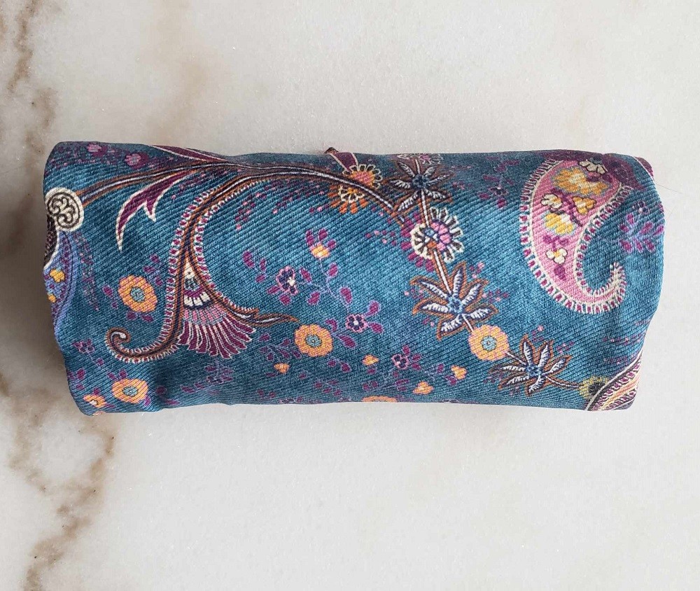 A blue ascot with orange and purple paisley designs is rolled up ready to be stored in a box