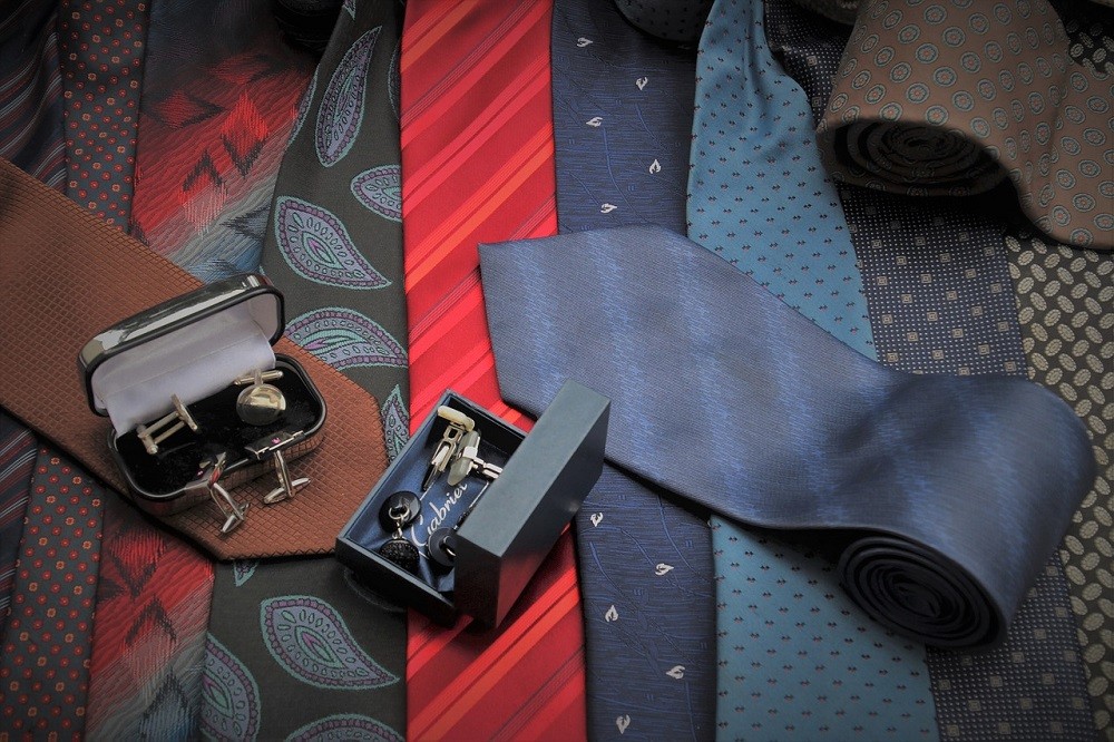 Various ties and cufflinks are laid out on a table. Most of the ties are blue and red with stripes, polka dots, and paisley patterns