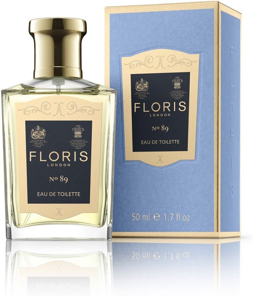 A bottle of Floris 89 cologne sits beside the light blue box it is shipped in. Both the bottle and box display a dark blue sticker with a gold border. The name of the fragrance house and scent are written inside the sticker