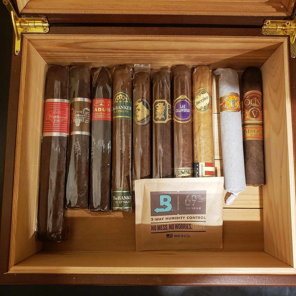 A variety of cigars are displayed in a desktop humidor. All of them are individually protected with a clear cellophane sleeve