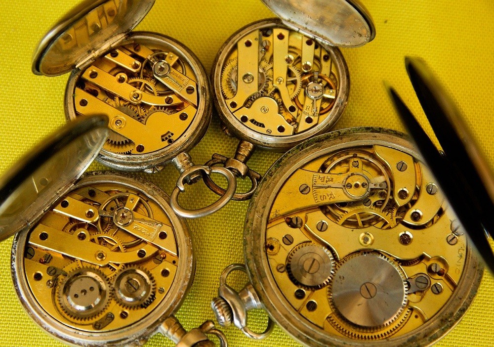 4 vintage pocket watches with their cases opened showing off brass movements likely from the 1800s