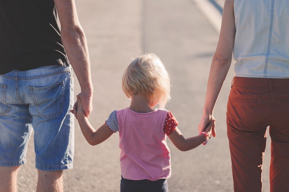A young child is walking between their parents holding each of their hands