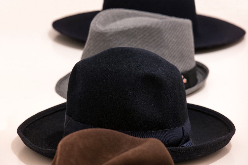 A grey, black, and brown fedora are lined up in a row