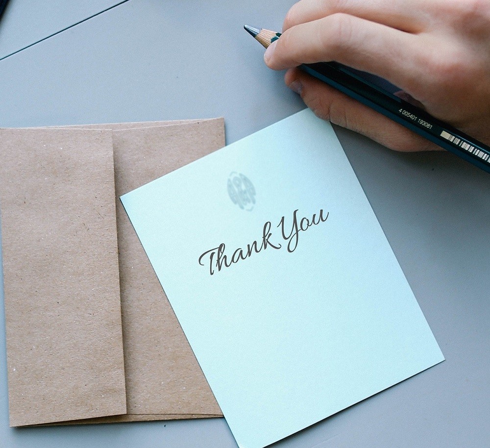 A Thank You note stationery set and someones hand with a pencil, ready to write in the card