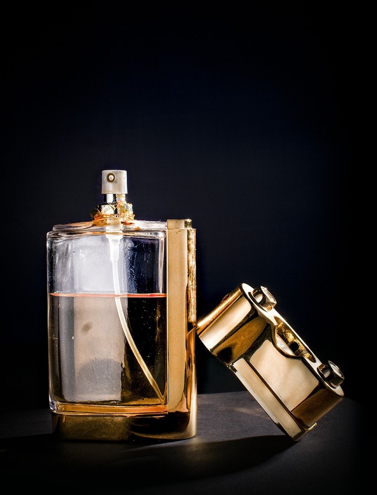 A clear bottle of unnamed cologne sits against a black backdrop. The cap to the bottle is propped up against it
