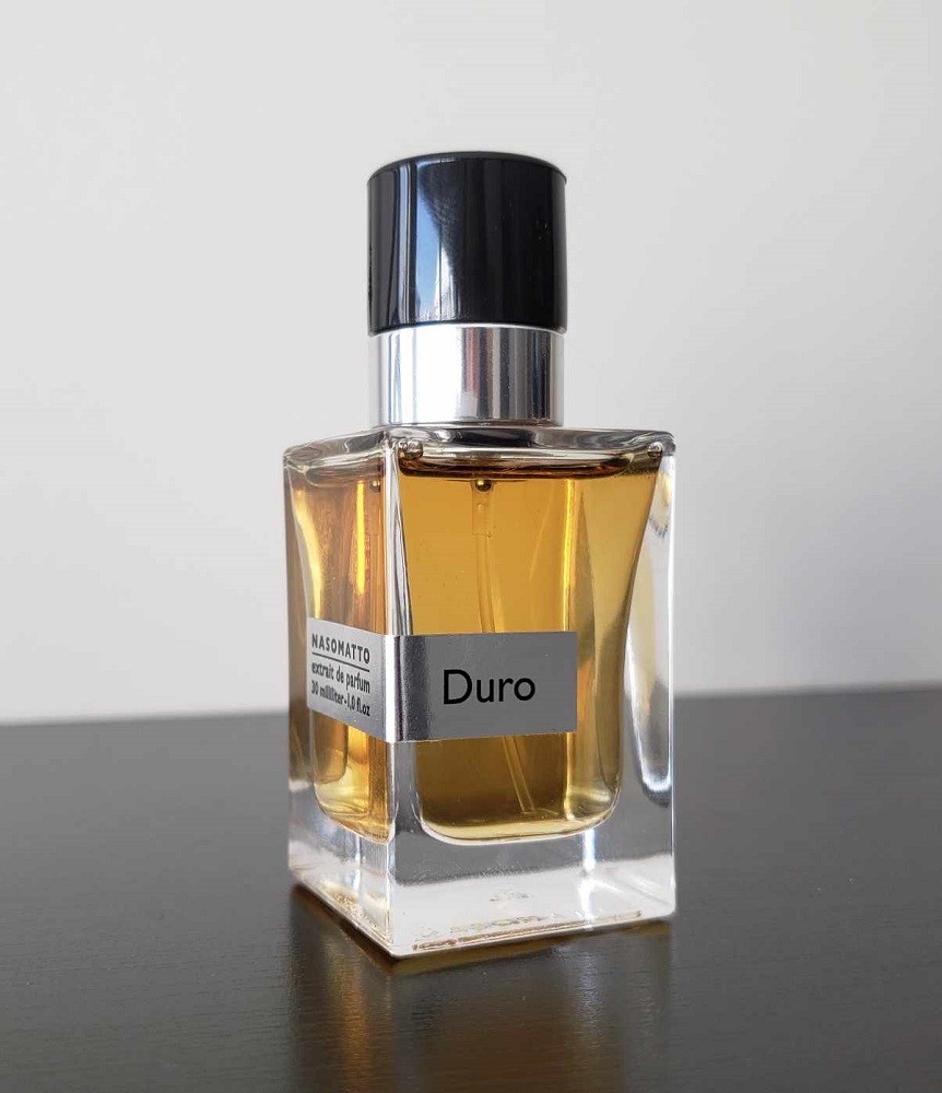 A bottle of light brown cologne called Duro with a small black travel cap on top