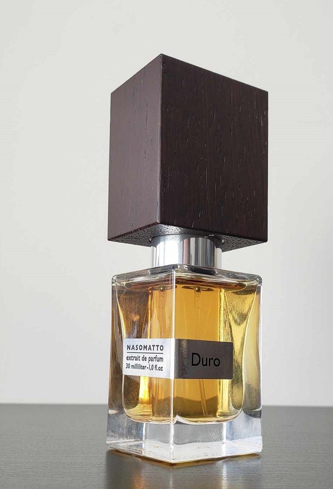 A bottle of light brown cologne in a square bottle and a large, black wooden cap. The cologne is called Duro and it's by a company called Nasomatto