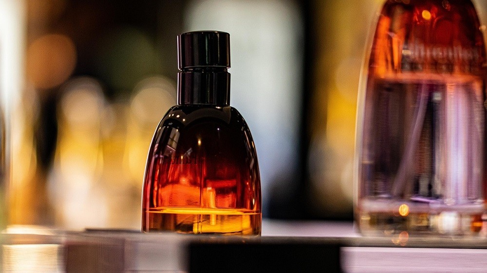 A round bottle of fragrance with a black top and orange/red bottle sits on a counter