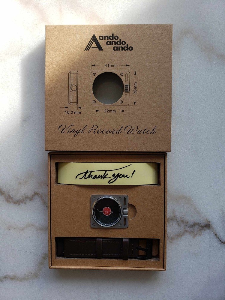 A front view of the box that contains the Vinyl Record Watch by AndoAndoAndo. The watch, strap, and stickers are nestled into cut-out molds inside the box