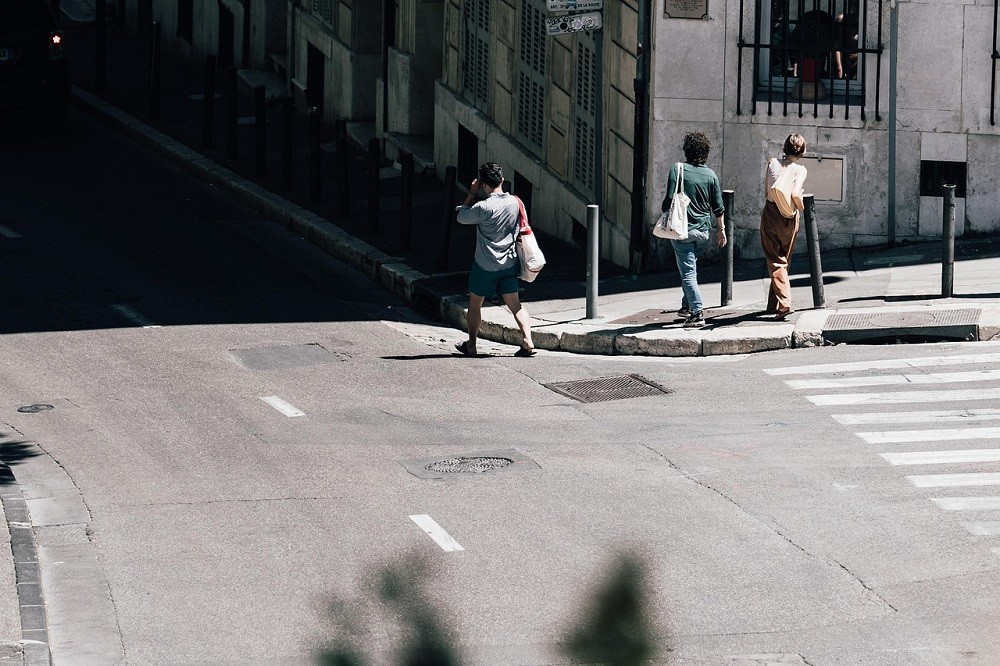 A man veers off from his friends who just stepped onto the sidewalk. He decided to walk on the road