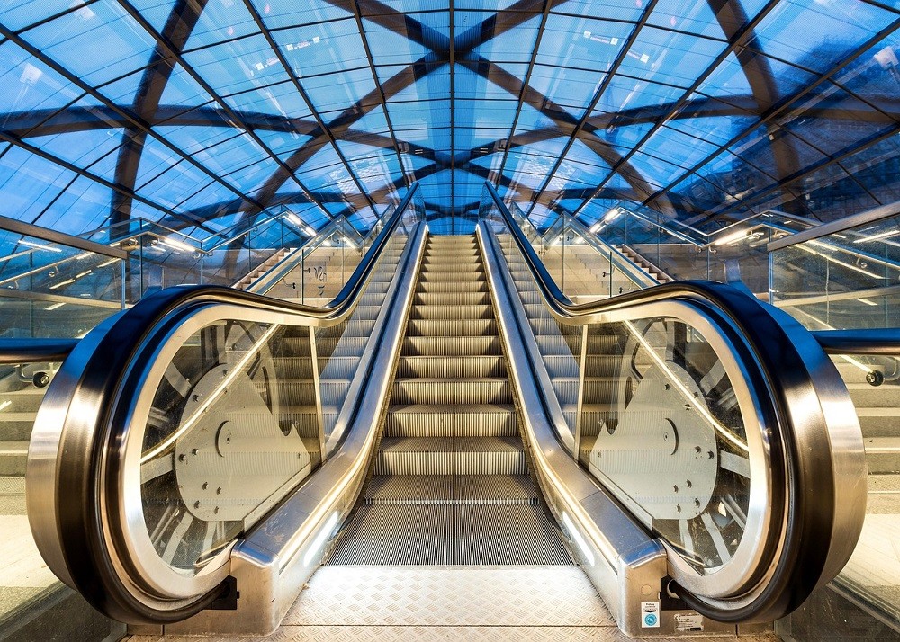 A front view of an empty escalator. It looks brand new. There is a large glass ceiling above it, showing a dark blue sky
