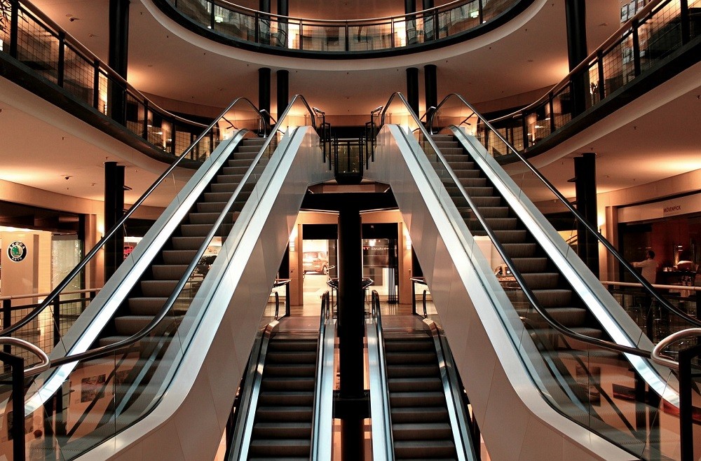 Four escalators are in this picture. They are located inside a 3 level mall. Two escalators go from the middle floor to the top floor and two from the bottom floor to the middle floor. No one is riding them