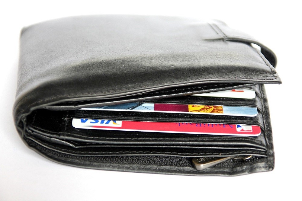 An overly stuffed wallet sits on a table. It is so full it can barely close