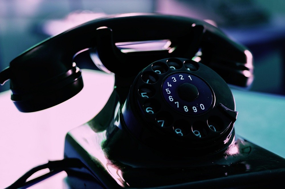 A black rotary phone sits on a desk